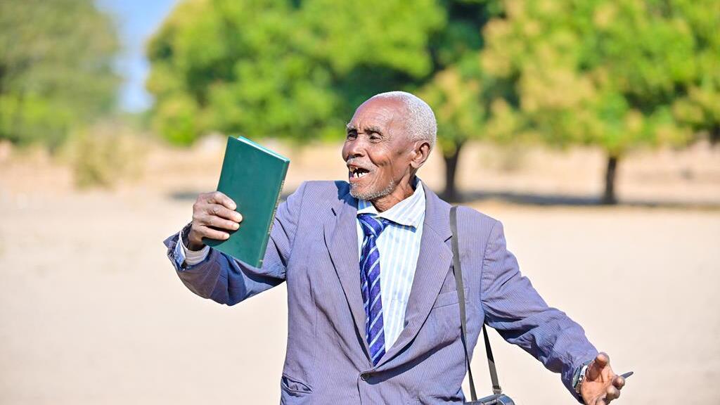 A elderly man celebrating seeing and holding the Kwamashi New testament Bible for the first time